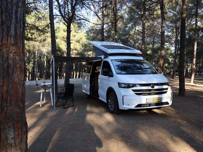 Ephesus auf dem VW Transporter der neuen Generation mit langem Radstand im Kiefernwald, Aufstelldach und Markise geöffnet