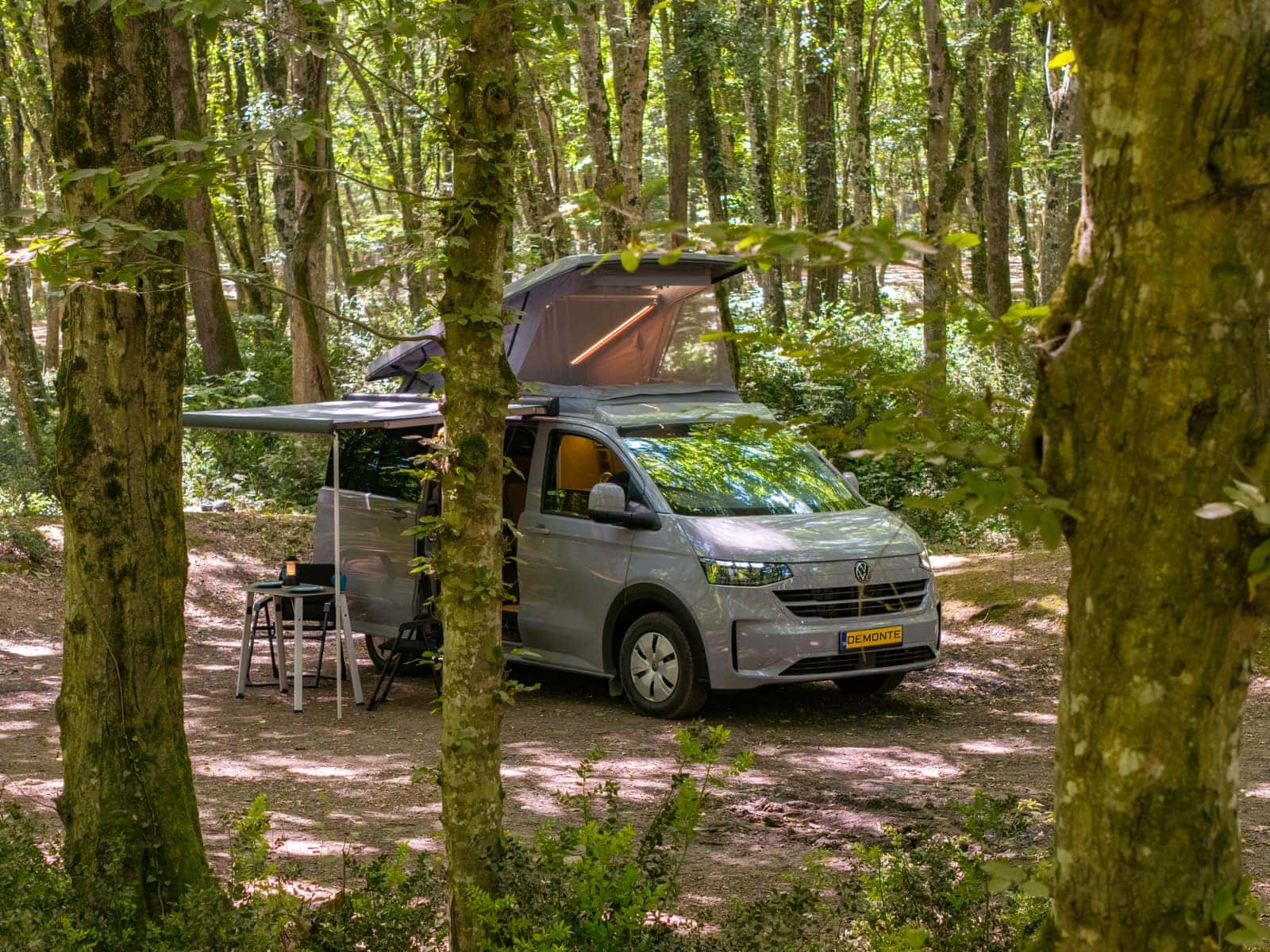 New Cappadocia auf dem VW Transporter der neuen Generation im Wald, Aufstelldach und Markise geöffnet, Campingtisch darunter