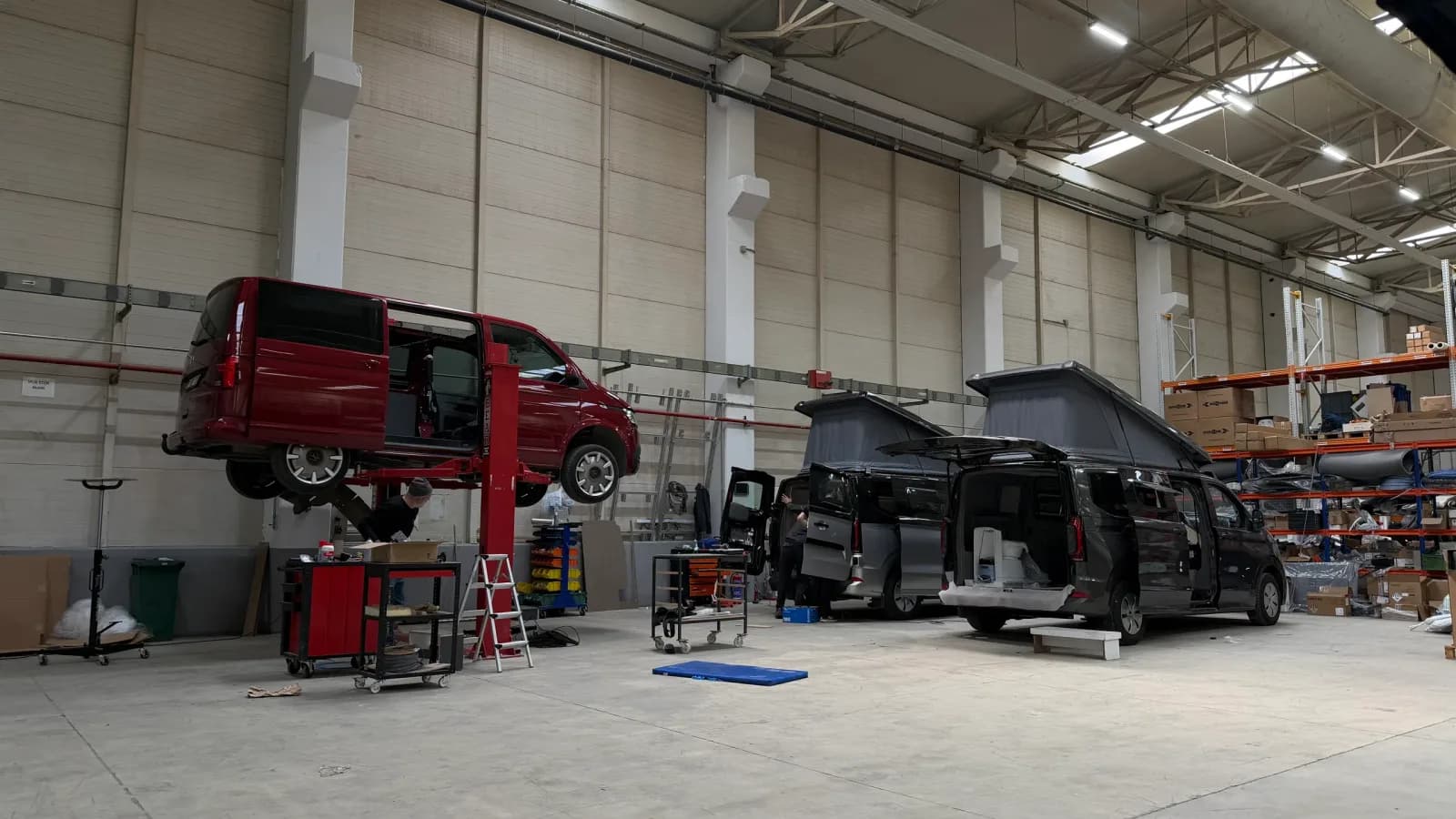 Ein VW Transporter auf der Hebebühne und zwei Ford Transit Custom im Ausbau mit aufgestelltem Aufstelldach in der Produktionsstätte