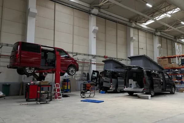 Ein VW Transporter auf der Hebebühne und zwei Ford Transit Custom im Ausbau mit aufgestelltem Aufstelldach in der Produktionsstätte