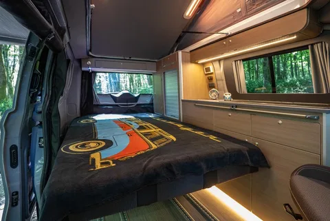 Die zum Bett umgebaute Bank mit ausgelegter Decke, durch das Seitenfenster ist der Wald zu sehen