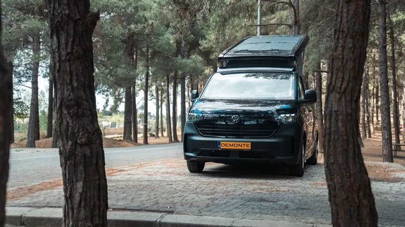 Die Front des Olympos zwischen zwei Kiefernstämmen: Kühlergrill des Transporters der neuen Generation und aufgestelltes Dach