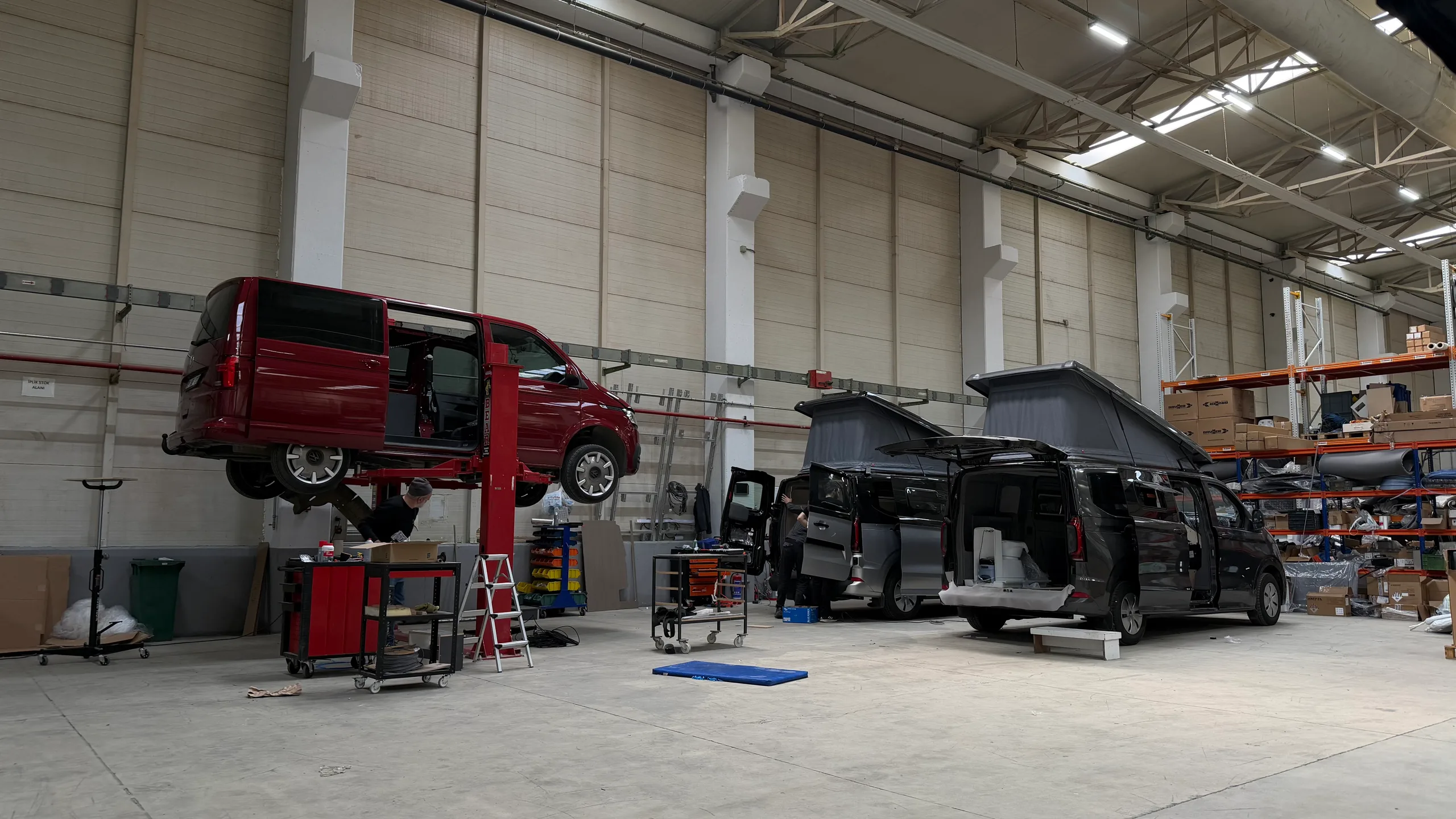 Ein VW Transporter auf der Hebebühne und zwei Ford Transit Custom im Ausbau mit aufgestelltem Aufstelldach in der Produktionsstätte Dilovasi