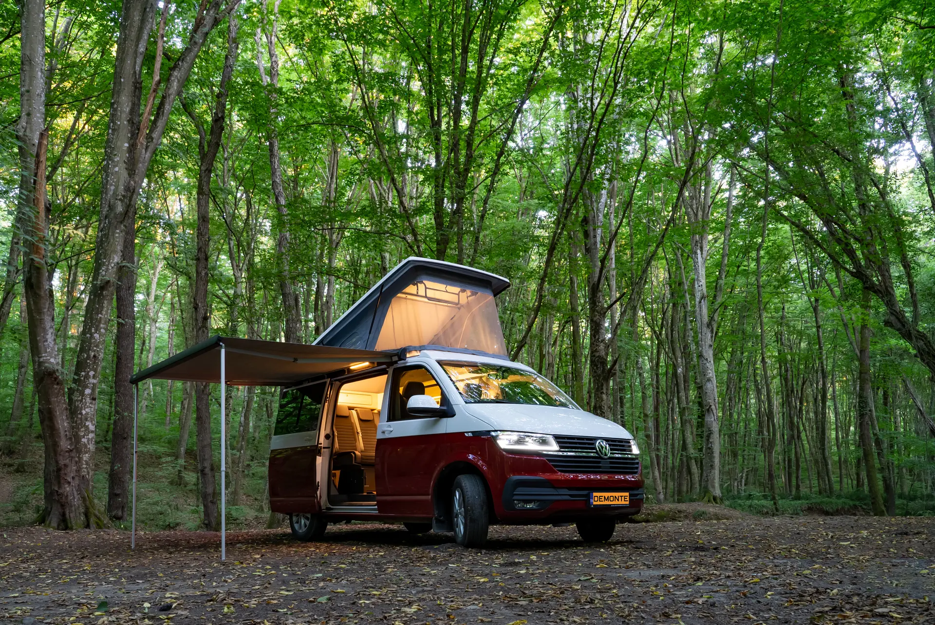 Zweifarbiger Demonte-Camper in Bordeaux und Weiß im Wald, Seitentür offen, Innenbeleuchtung sichtbar